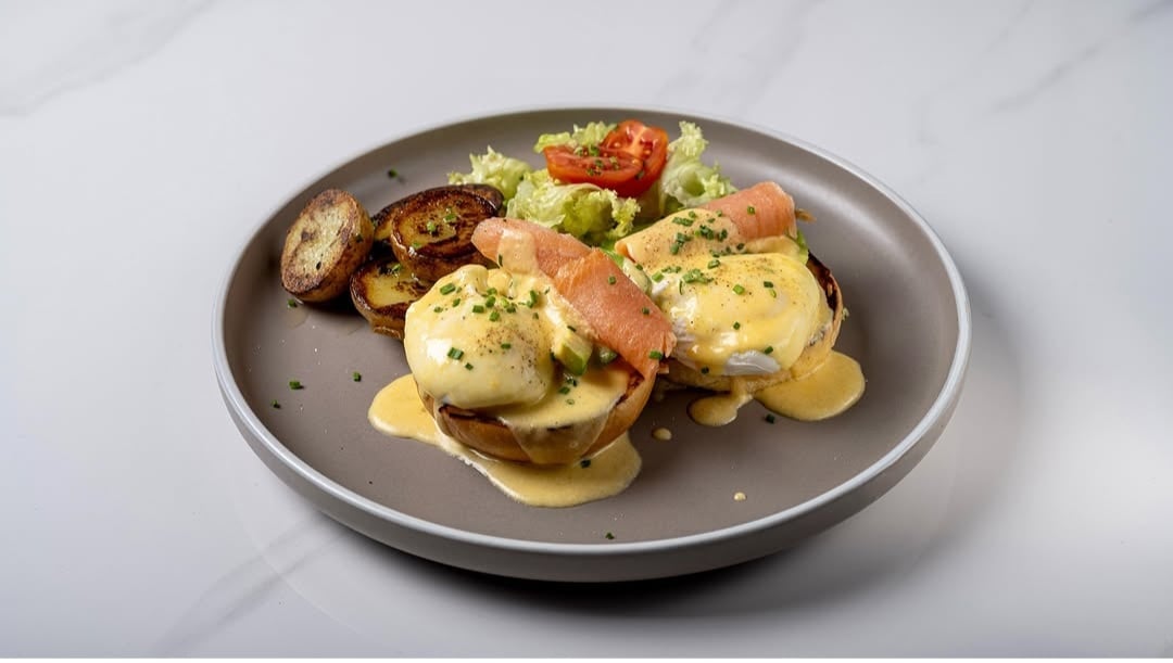 Plated Eggs Benedict with sliced potatoes and roasted vegetables on a gray ceramic plate