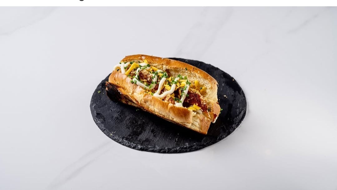 Gourmet hot dog with toppings on a black oval plate against a marble background